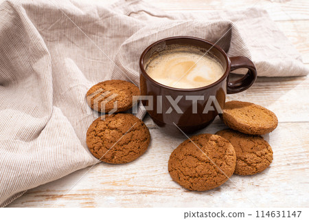 A cup of aromatic coffee cappuccino with Oatmeal cookies. Morning rays and latte for breakfast in a beautiful brown cup. Wooden background. 114631147