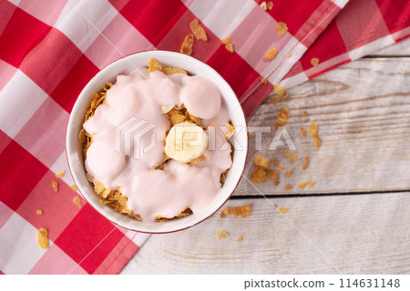 Healthy breakfast. Muesli with yogurt and banana on a light wooden background with a red tablecloth. View from above. Copy space. 114631148