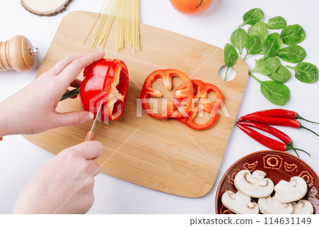 Cooking vegetables, healthy cooking. The process of slicing bell peppers. Mushrooms mushrooms, spinach leaves, chili peppers and spaghetti on a white background. Cutting board. Chef 114631149