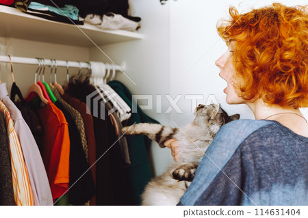 red-haired teenage girl and big cat choose things from closet 114631404