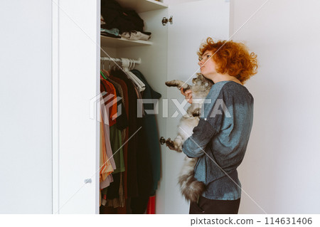 red-haired teenage girl and big cat choose things from closet red-haired teenage girl and big cat choose things from closet 114631406