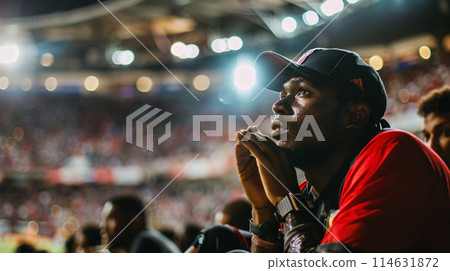 a soccer fan, their face a mask of concentration as they watch the game with rapt attention, hands clasped tightly in front of them 114631872