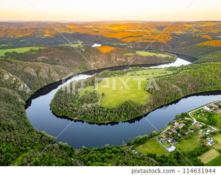 Aerial view of the Solenice Horseshoe Bend on the Vltava River in Czechia, showcasing the winding river surrounded by lush greenery and a small village during a picturesque sunset. Aerial view of the Solenice Horseshoe Bend on the Vltava River in Czechia, showcasing the winding river surrounded by lush greenery and a small village during a picturesque sunset. 114631944