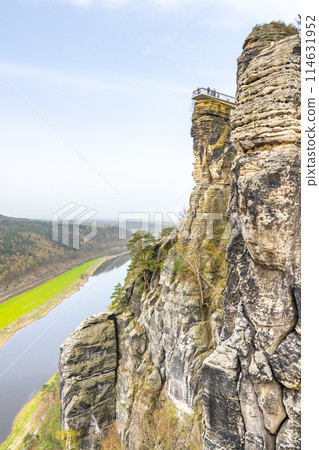 Overlooking the serpentine Elbe River, a visitor enjoys the vista from Bastei Bridge in Saxon Switzerland National Park. Kurort Rathen, Germany Overlooking the serpentine Elbe River, a visitor enjoys the vista from Bastei Bridge in Saxon Switzerland National Park. Kurort Rathen, Germany 114631952