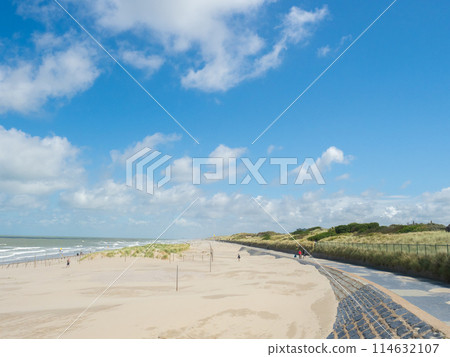 Oostende, Belgium - August 1st 2023: The beach promenade and dunes at the coast close to the city. Oostende, Belgium - August 1st 2023: The beach promenade and dunes at the coast close to the city. 114632107