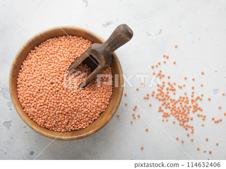 Dry raw orange lentils seeds in wooden bowl with scoop on light table. Dry raw orange lentils seeds in wooden bowl with scoop on light table. 114632406