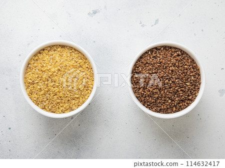 Ceramic bowls with brown and yellow bulgur dry raw seeds on kitchen table. Ceramic bowls with brown and yellow bulgur dry raw seeds on kitchen table. 114632417