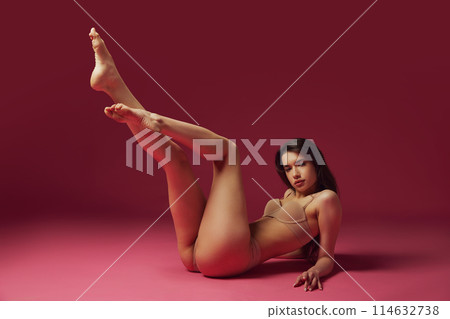 Beautiful young brunet girl with slim perfect body shape posing in beige underwear against magenta studio background 114632738