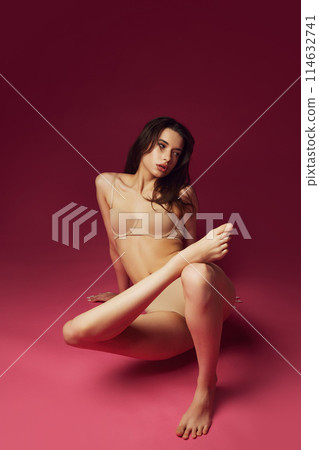 Beautiful young brunet girl with slim perfect body shape posing in beige underwear against magenta studio background 114632741