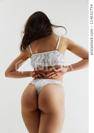 Back view image of elegant woman with slim fit body shape, buttocks posing in white lingerie isolated on grey studio background Back view image of elegant woman with slim fit body shape, buttocks posing in white lingerie isolated on grey studio background 114632754