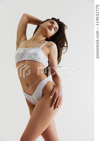 Sensuality and femininity vibe. Beautiful young woman in white elegant lingerie, with slim body posing isolated on grey studio background Sensuality and femininity vibe. Beautiful young woman in white elegant lingerie, with slim body posing isolated on grey studio background 114632778