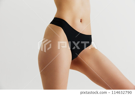 Healthy nutrition and massage body care. Cropped image of slim female body in black underwear, with slim waist, slender legs isolated on grey studio background 114632790
