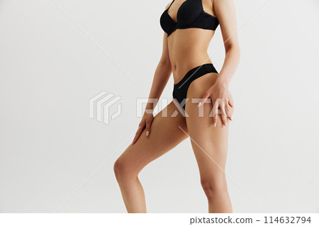 Cropped image of beautiful female body, slender legs, fit buttocks and slim waist. Model posing in underwear isolated on grey studio background 114632794