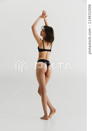 Full-length image of young brunette girl with slim, fit body, posing in black lingerie isolated on grey studio background Full-length image of young brunette girl with slim, fit body, posing in black lingerie isolated on grey studio background 114632806