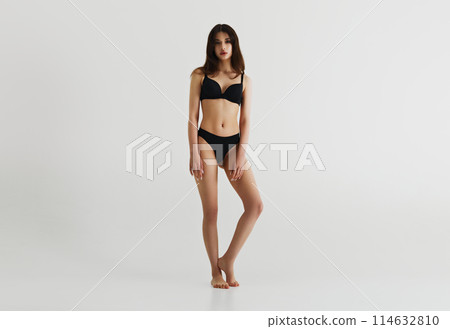 Full-length image of beautiful young female model with perfect slim body, posing in black underwear isolated on grey studio background Full-length image of beautiful young female model with perfect slim body, posing in black underwear isolated on grey studio background 114632810
