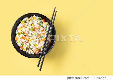 White rice with vegetables in a black bowl on yellow background 114633309