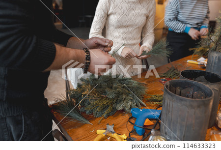A young woman creating a Christmas wreath at a festive decoration workshop. 114633323