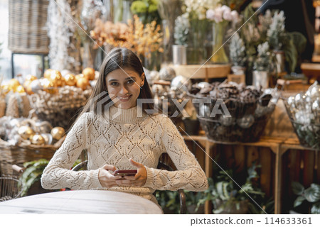 A captivating, colorful girl admiring Christmas decor and browsing her smartphone. A captivating, colorful girl admiring Christmas decor and browsing her smartphone. 114633361