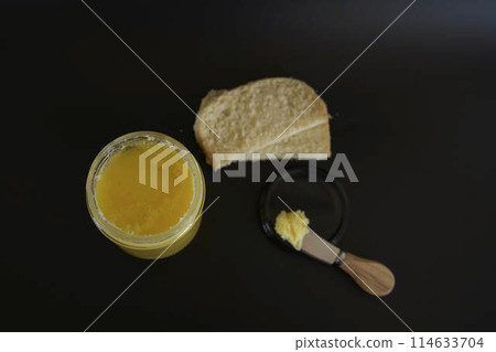 butter ghee in a transparent jar with homemade bread on a black background butter ghee in a transparent jar with homemade bread on a black background 114633704