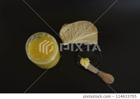 butter ghee in a transparent jar with homemade bread on a black background butter ghee in a transparent jar with homemade bread on a black background 114633705