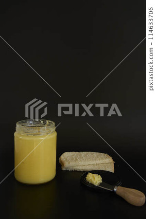 butter ghee in a transparent jar with homemade bread on a black background butter ghee in a transparent jar with homemade bread on a black background 114633706