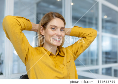 Relaxed businesswoman smiling confidently while stretching in an office environment. Displaying positive energy and professional comfort in a modern workspace. Relaxed businesswoman smiling confidently while stretching in an office environment. Displaying positive energy and professional comfort in a modern workspace. 114633755