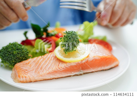 Asian elderly woman patient eating salmon stake and vegetable salad for healthy food in hospital. Asian elderly woman patient eating salmon stake and vegetable salad for healthy food in hospital. 114634111