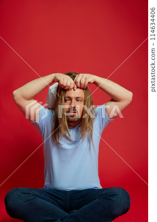 Dad with his daughter's hair draped over his head, creating funny and playful moment against vibrant red background. 114634406