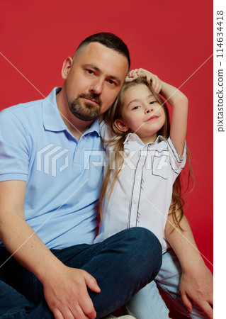 Portrait of father with his little beloved daughter dressed casual clothes posing against vibrant red background. Portrait of father with his little beloved daughter dressed casual clothes posing against vibrant red background. 114634418
