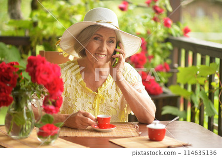 Happy aged woman drinking coffee and talking on phone 114635136