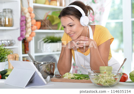 Portrait of beautiful young woman making salad and listening to music Portrait of beautiful young woman making salad and listening to music 114635154