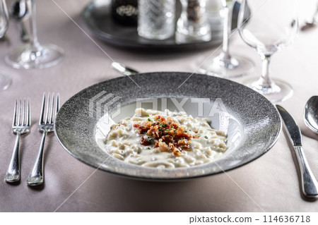 Halusky as traditional Slovak potato gnocchi with sheep cheese bryndza, fried bacon and chives served in a modern plate and on a festively laid restaurant table. 114636718