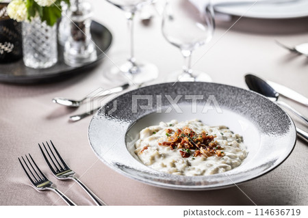 Halusky as traditional Slovak potato gnocchi with sheep cheese bryndza, fried bacon and chives served in a modern plate and on a festively laid restaurant table. 114636719