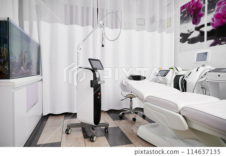 Interior of beautician cabinet with modern cosmetology equipment for skincare rejuvenation treatment and salon chair. Radiofrequency microneedling device, patient daybed and laser machine in clinic. 114637135