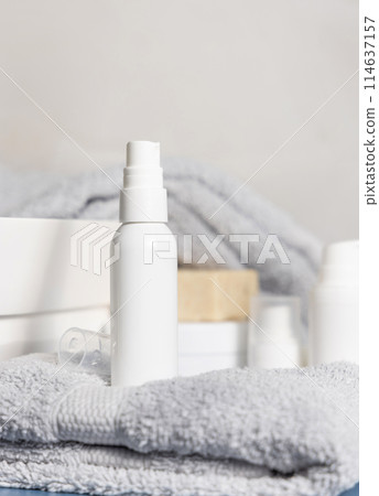 White blank spray bottle on grey folded towel near other cosmetics and basin, mockup 114637157