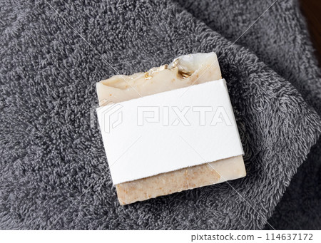 Beige handmade soap bar with blank label on dark grey folded towel top view, mockup Beige handmade soap bar with blank label on dark grey folded towel top view, mockup 114637172