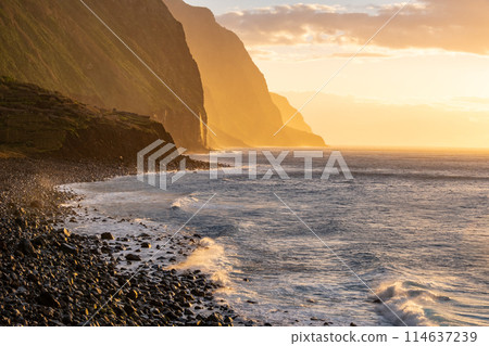Volcanic rock cliffs Achadas da Cruz in backlit sunlight. Waves of the Atlantic Ocean. Beautiful sunset seascape of the resort island of Madeira, Portugal Volcanic rock cliffs Achadas da Cruz in backlit sunlight. Waves of the Atlantic Ocean. Beautiful sunset seascape of the resort island of Madeira, Portugal 114637239
