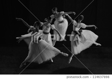 Black and white photo of young female ballet dancers in synchronized motion, their white tutus creating fluid harmony of blurred elegance 114637898