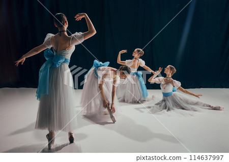 Four ballet dancers in flowing white costumes with blue ribbons, gracefully poised in different ballet positions. 114637997