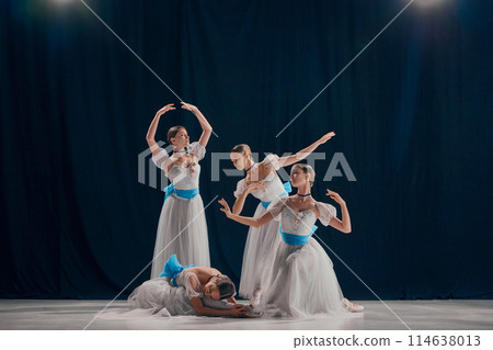 Four ballerinas, poised in white tutus with blue sashes, exhibit their refined ballet technique against dark backdrop on stage. Four ballerinas, poised in white tutus with blue sashes, exhibit their refined ballet technique against dark backdrop on stage. 114638013