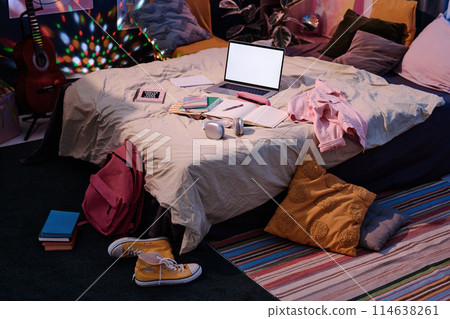 High angle view of part of teenagers bedroom interior with laptop, clothes and notebooks on bed, no people shot High angle view of part of teenagers bedroom interior with laptop, clothes and notebooks on bed, no people shot 114638261