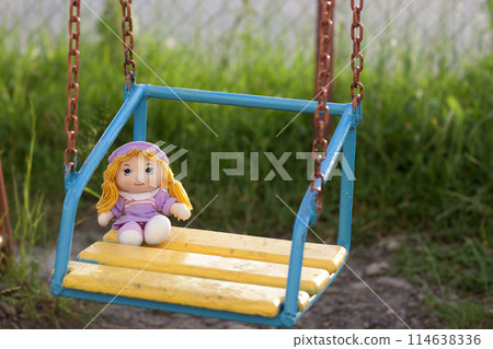 Little hand made doll seating on yellow wooden bench in bright summer day 114638336