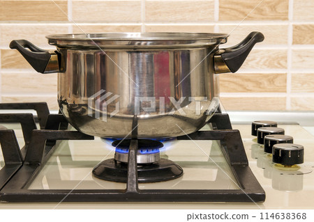 Metal cooking pot standing on kitchen stove with flame. 114638368