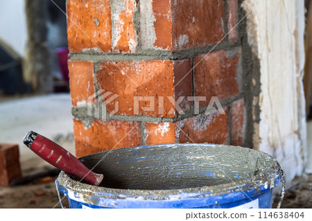 Close up of bricklaying industrial installing bricks on construction site wall with working tools, mortar, level 114638404