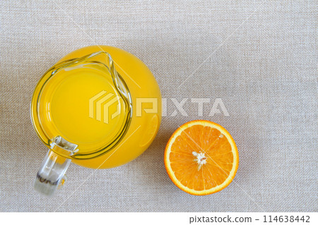 Jug and glass of orange juice and ripe oranges from above, top view on burlap sackcloth background 114638442