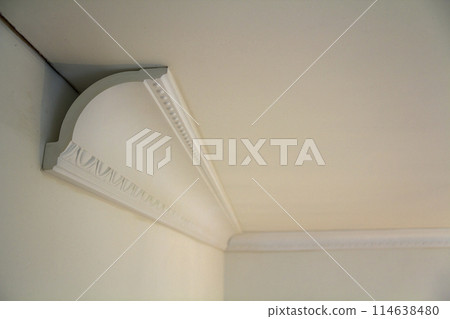 Close-up detail of decoration white molding connected with glue adhesive to wall and ceiling in interior room renovation and reconstruction. Close-up detail of decoration white molding connected with glue adhesive to wall and ceiling in interior room renovation and reconstruction. 114638480
