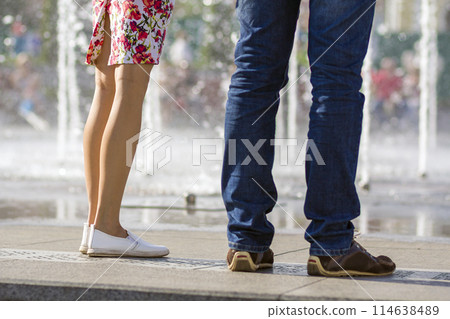 Close up of two pairs of legs, girl in short dress with floral pattern and white shoes and man in blue jeans and brown shoes,standing together on blurred colorful background. Close up of two pairs of legs, girl in short dress with floral pattern and white shoes and man in blue jeans and brown shoes,standing together on blurred colorful background. 114638489