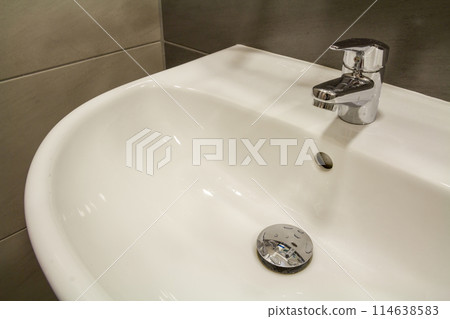 Close-up of new modern ceramic clean empty white washbasin sink connected to the sewer on background of nice light beige ceramic tiles. Professional plumbing and installation concept. 114638583