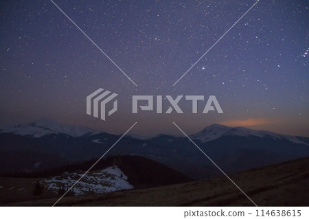 Majestic view of fantastic starry dark sky over magnificent Carpathian mountains covered with evergreen forest and snow-capped peaks in distance. Breathtaking panorama of beauty and magic of nature. 114638615