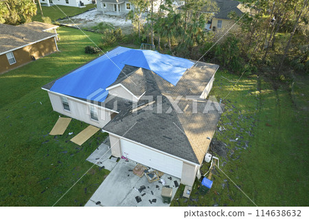 Aerial view of damaged in hurricane Ian house roof covered with blue protective tarp against rain water leaking until replacement of asphalt shingles 114638632